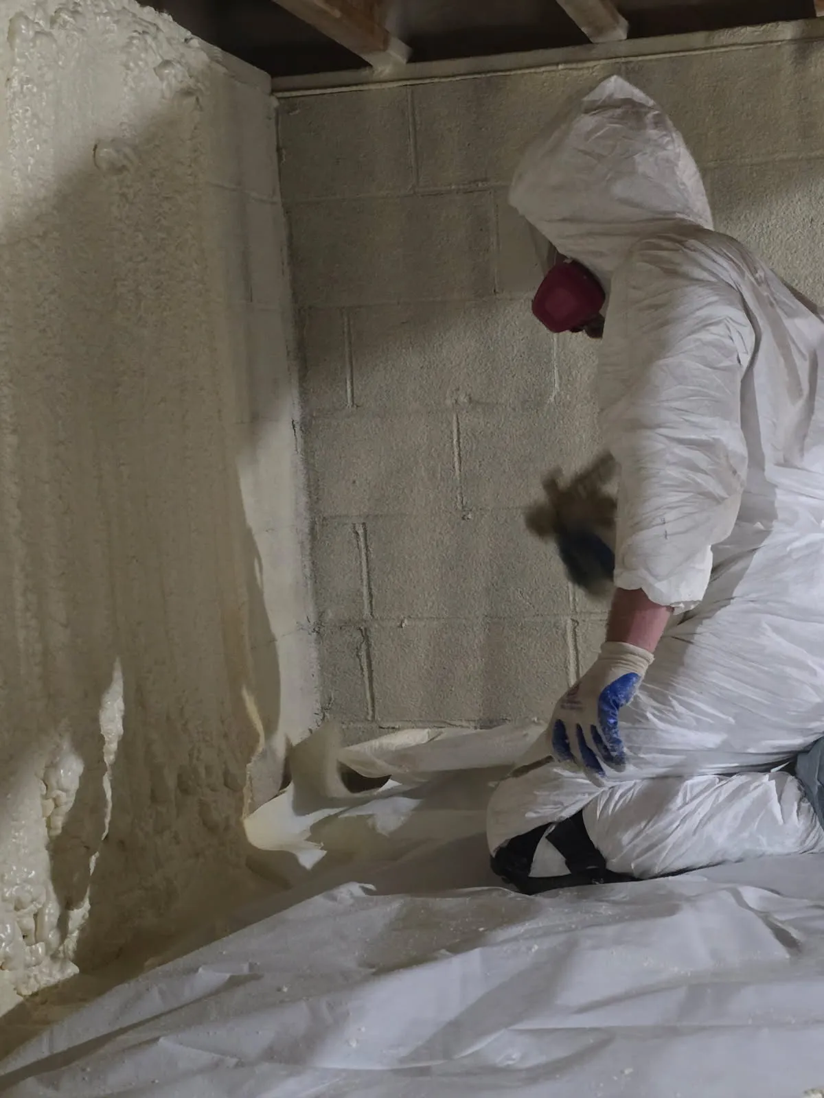 Worker applying spray foam to crawl space cinder block wall